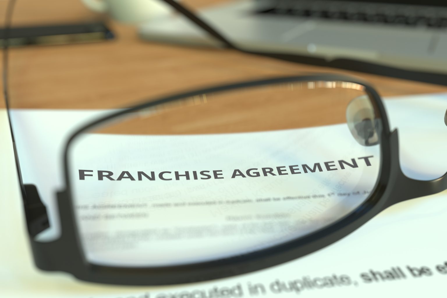 Copy of a franchise agreement behind glasses on a desk, 3D rendering Franchise Agreements