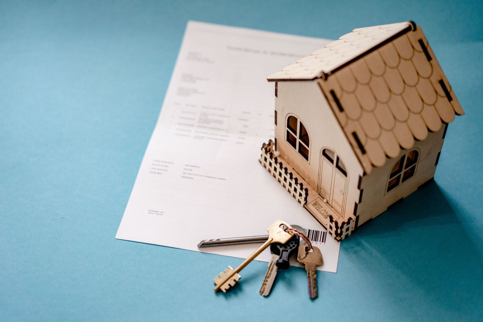 5-ways-technology-can-make-real-estate-closings-more-efficient A miniature wooden house model and a set of keys resting on a property contract