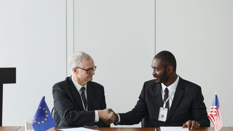 Two executives shake hands across a negotiating table set with EU and US flags, illustrating winning Strategies for Resolving International Business Disputes Across Borders